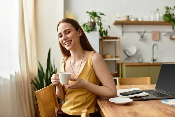 A young beautiful woman smiles brightly while holding a coffee cup in a well lit kitchen. — Stock Photo