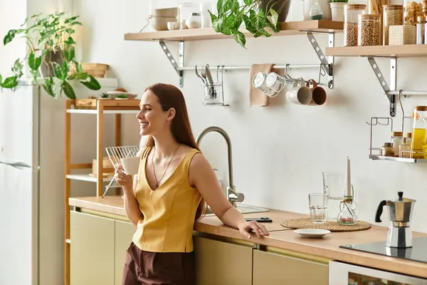 A young woman enjoys a drink in her stylish kitchen, surrounded by greenery. — Stock Photo