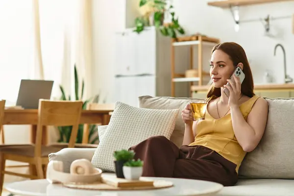 Relaxed young woman sips tea and chats on the phone in a cozy living room filled with greenery. — Stock Photo