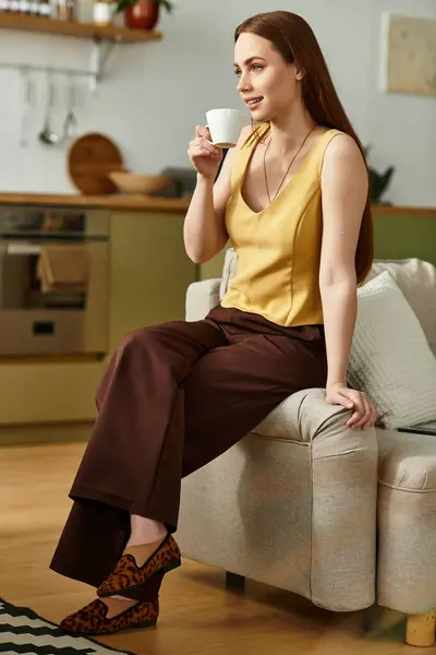 A radiant woman relaxes on a sofa, enjoying a warm drink in her stylish kitchen. — Stock Photo