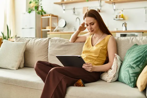 Eine junge Frau entspannt sich auf einem Sofa mit ihrem Tablet in einem warmen, einladenden Raum. — Stockfoto