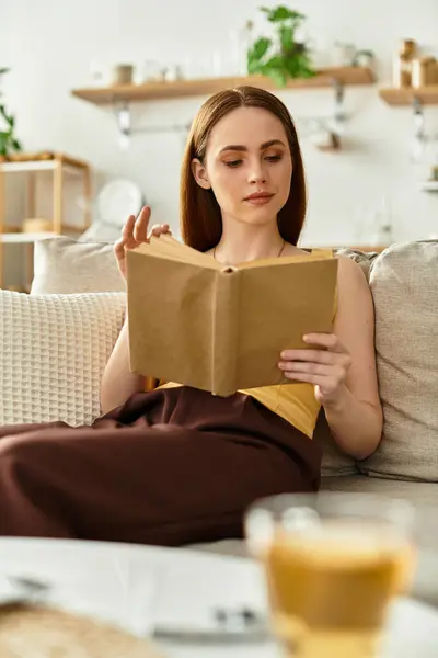 Una joven se sienta cómodamente en su acogedora sala de estar, leyendo atentamente un libro. — Stock Photo