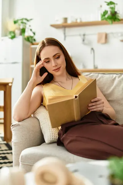 A young woman relaxes on a cozy sofa, absorbed in her book in a warm setting. — Stock Photo