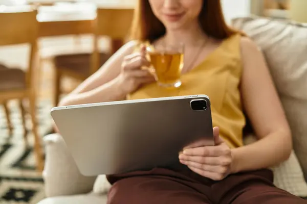 Young woman enjoys her tea while browsing on a tablet, immersed in a tranquil afternoon atmosphere. — Stock Photo