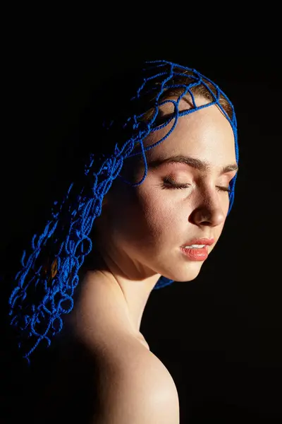 Young woman with closed eyes showcases a unique blue headpiece against dark background. — Stock Photo