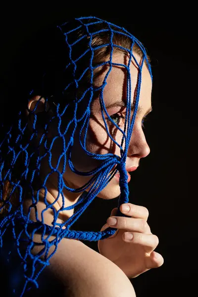 A young woman poses with blue netting on her face, contrasting beautifully with the dark. — Stock Photo