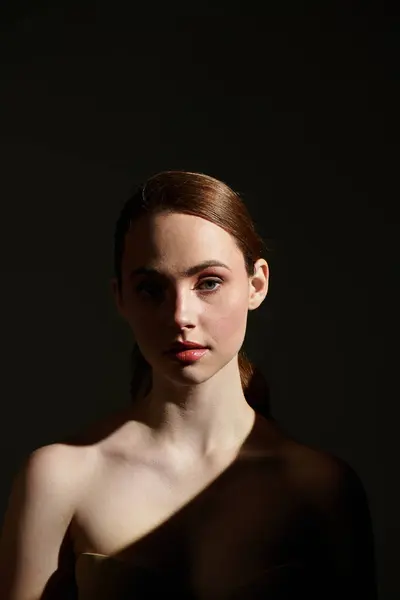 A young woman with striking features stands confidently, her face softly glowing in the light. — Stock Photo