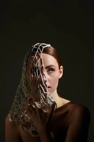 A young woman holds a mesh veil against her face, creating an intriguing blend of light and shadow. — Stock Photo