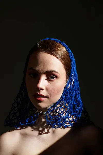 A young beauty wears a striking blue headpiece as shadows dance around her. — Stock Photo