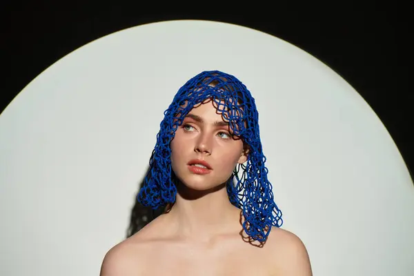 A young woman wears a unique blue headpiece, radiating elegance against a bold backdrop. — Stock Photo