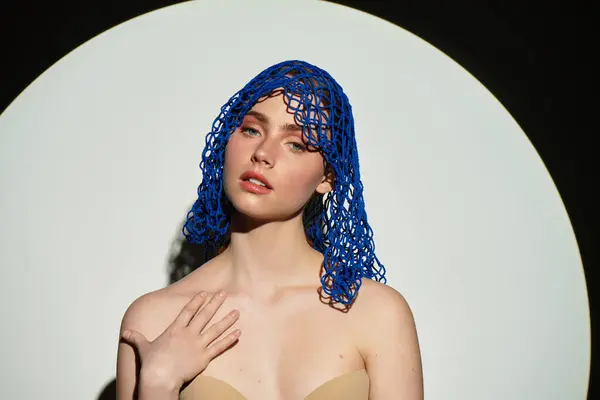 A stunning young woman poses gracefully with a creative blue headpiece, framed by soft lighting. — Stock Photo