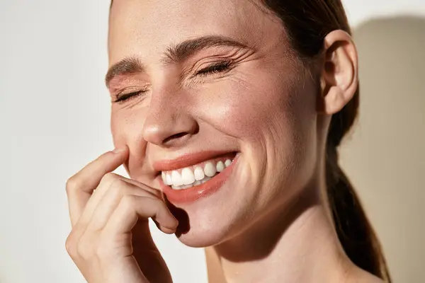 A young woman grins in warm sunlight, playfully touching her cheek and exuding joy. — Stock Photo