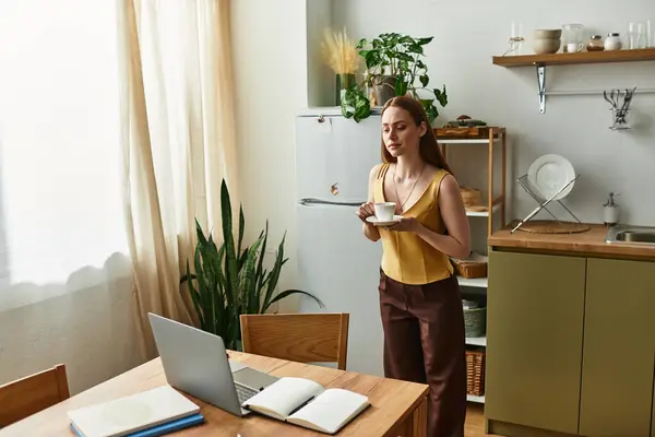 A young woman enjoys coffee in a bright kitchen while focused on her laptop. — Stock Photo