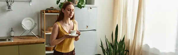 A young beautiful woman holds a cup of tea while basking in sunlight in her inviting kitchen. — Stock Photo