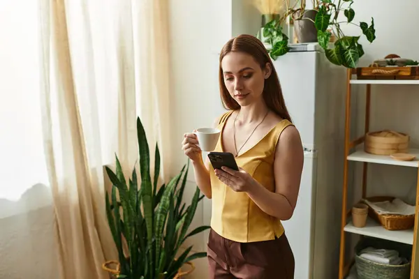 A young woman sips coffee, glancing at her phone in a bright room with green plants. — Stock Photo