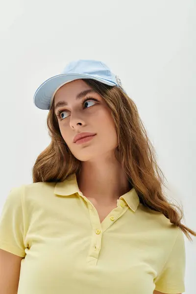 A young woman with wavy hair casually wears a light yellow shirt and a blue cap, lost in thought. — Stock Photo