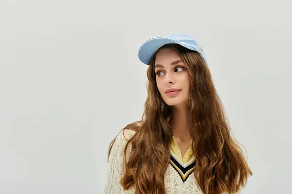 A young woman in a cozy sweater and light blue cap pauses thoughtfully against a neutral backdrop. — Stock Photo