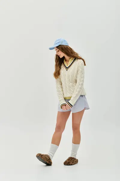 A young woman in a stylish sweater and shorts exudes playfulness in a simple setting. — Stock Photo