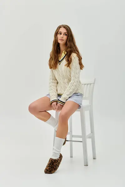 A confident young woman with long hair poses elegantly in stylish attire on a chair. — Stock Photo
