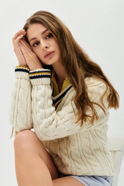 Una giovane donna in un maglione accogliente poggia il mento sulle mani, cercando sereno. — Foto stock