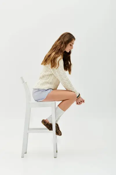 A young woman sits thoughtfully on a white chair, wearing a serene expression. — Stock Photo