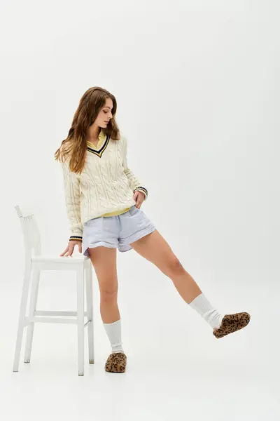 In a bright studio, a young woman in a sweater and shorts strikes a playful pose. — Stock Photo
