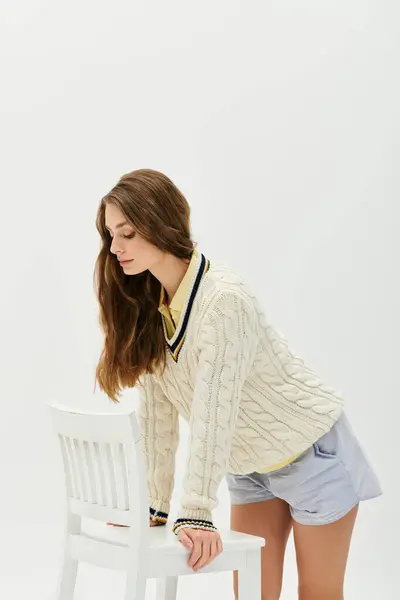 Frau mit langen Haaren lehnt auf weißem Stuhl in minimalistischem Atelier und strahlt jugendlichen Stil aus. — Stockfoto