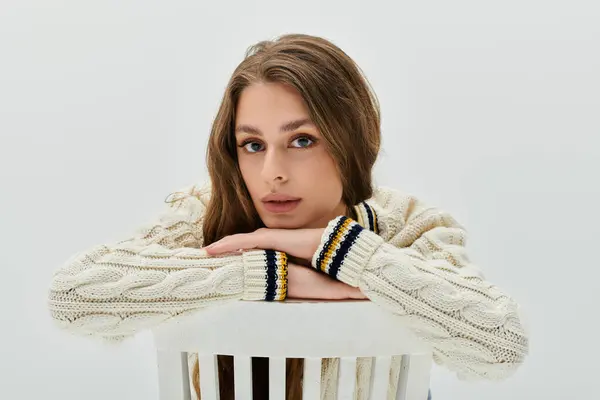 A young woman leans on a white chair, exuding charm and confidence in a serene setting. — Stock Photo