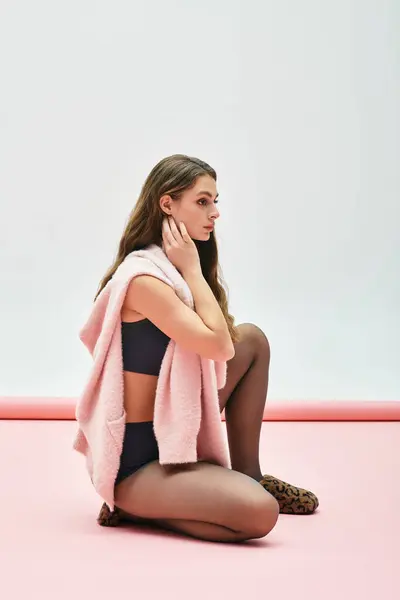 A young woman sits elegantly on a soft pink floor, radiating confidence in stylish casual wear. — Stock Photo