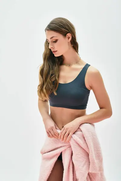 Una mujer joven elegante en un suéter rosa suave se levanta pensativamente, exudando elegancia y aplomo. - foto de stock