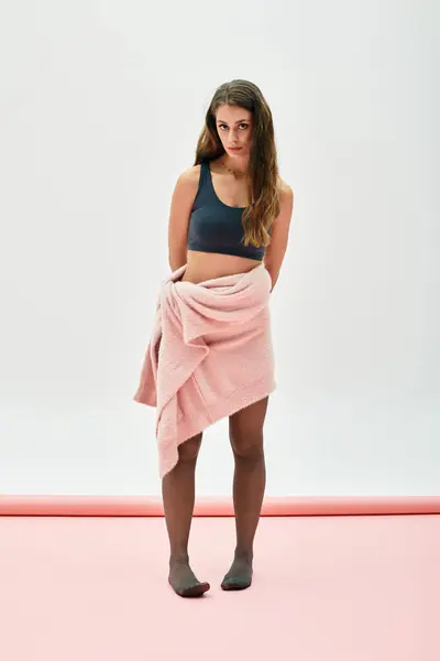 A beautiful young woman stands confidently with a towel draped around her, striking a poised pose. — Stock Photo