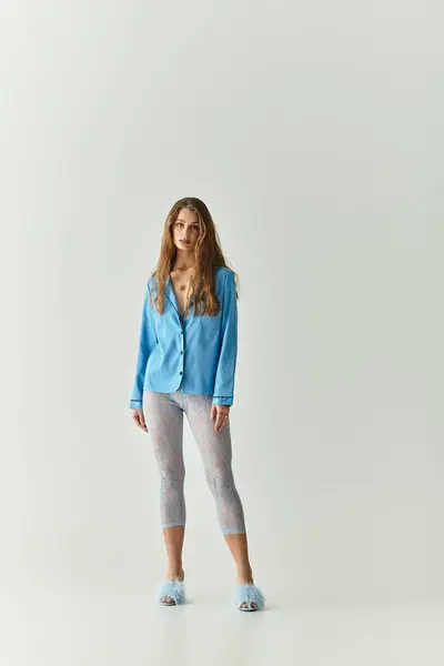A young woman confidently poses in a light room, wearing a blue cardigan and stylish leggings. — Stock Photo
