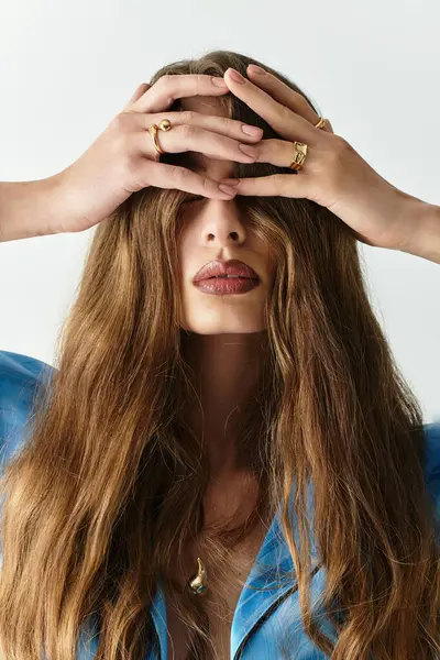 Una joven muestra su belleza, ocultando su rostro con el pelo largo y fluido y las manos delicadas. - foto de stock