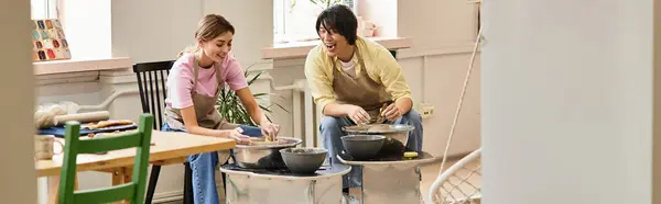 A young couple joyfully shapes clay on their wheels in a pottery studio. — Stock Photo