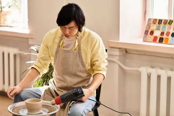 An artist uses a hair dryer to shape pottery while surrounded by inspiration and natural light — Stock Photo