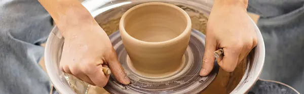 Hands skillfully shape wet clay into an elegant pot, surrounded by creative tools and art. — Stock Photo