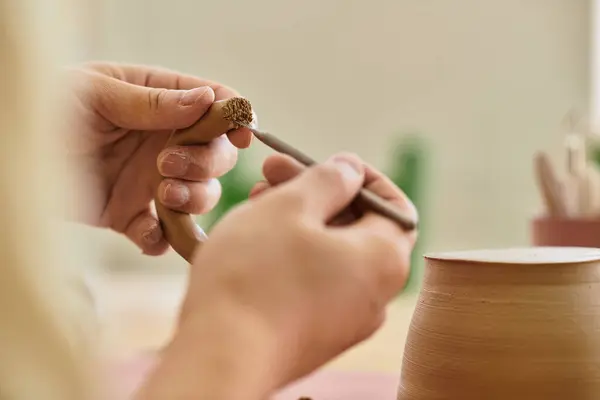 Hands shape and refine a clay piece, showcasing creativity in a well lit pottery studio. — Stock Photo