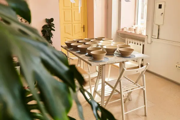 Estúdio de cerâmica com tigelas artesanais em uma mesa, rodeado por decoração artística e plantas. — Fotografia de Stock