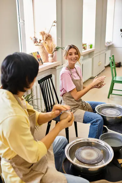 A young couple laughs and shapes clay together in a pottery studio. — Stock Photo