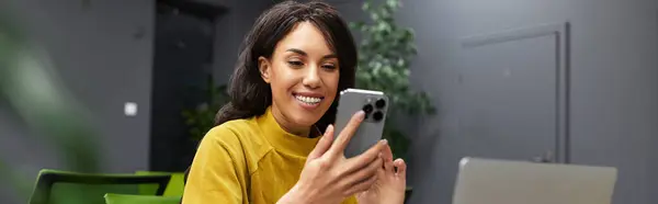A beautiful and elegant woman smiles at her smartphone while sitting at a contemporary office desk. — Stock Photo