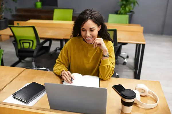 Una bella donna sta lavorando diligentemente alla sua scrivania in un ufficio elegante, sorridendo mentre digita. — Foto stock