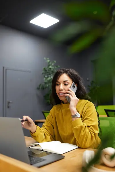 Young woman communicates over the phone while focused on notes and a laptop in a stylish workspace. — Stock Photo