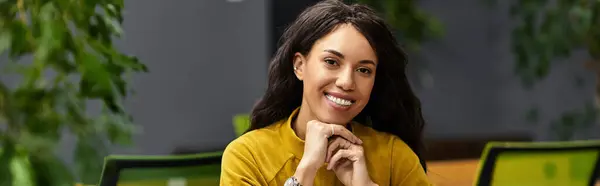 Una giovane donna elegante sorride mentre si concentra sul suo lavoro in un ufficio luminoso e invitante. — Foto stock