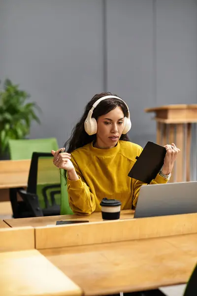 Giovane professionista che indossa le cuffie lavora diligentemente sul suo computer portatile mentre prende appunti. — Stock Photo