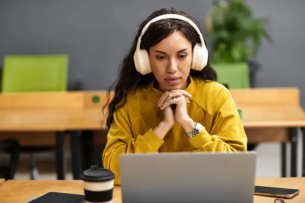 Beautiful woman wearing headphones works intently on her laptop in a stylish office space. — Stock Photo