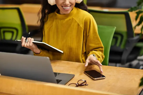 Giovane donna in abbigliamento elegante lavora diligentemente sul suo computer portatile durante l'utilizzo del suo smartphone. — Stock Photo