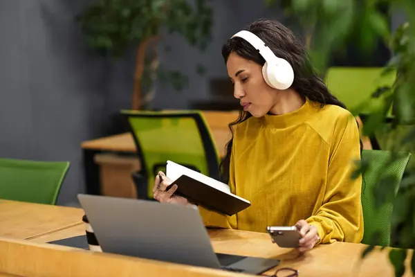 Dans un bureau animé, une femme en pull jaune prend des notes tout en appréciant la musique. — Photo de stock