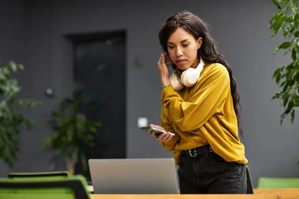 A beautiful woman in a chic outfit engages with her smartphone, surrounded by a stylish workspace. — Stock Photo