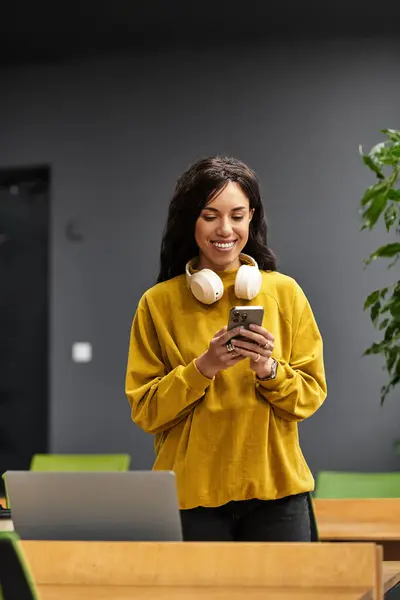 Mujer elegante sonríe mientras comprueba los mensajes en su teléfono en un entorno de oficina contemporáneo. — Stock Photo