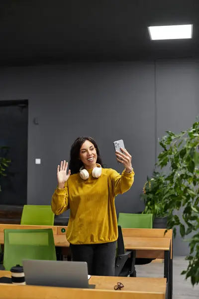 Beautiful young woman waves while participating in a virtual meeting in a stylish office setting. — Stock Photo